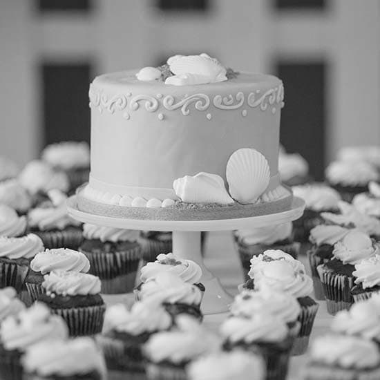 Celebration cake on a pedestal surrounded by cupcakes